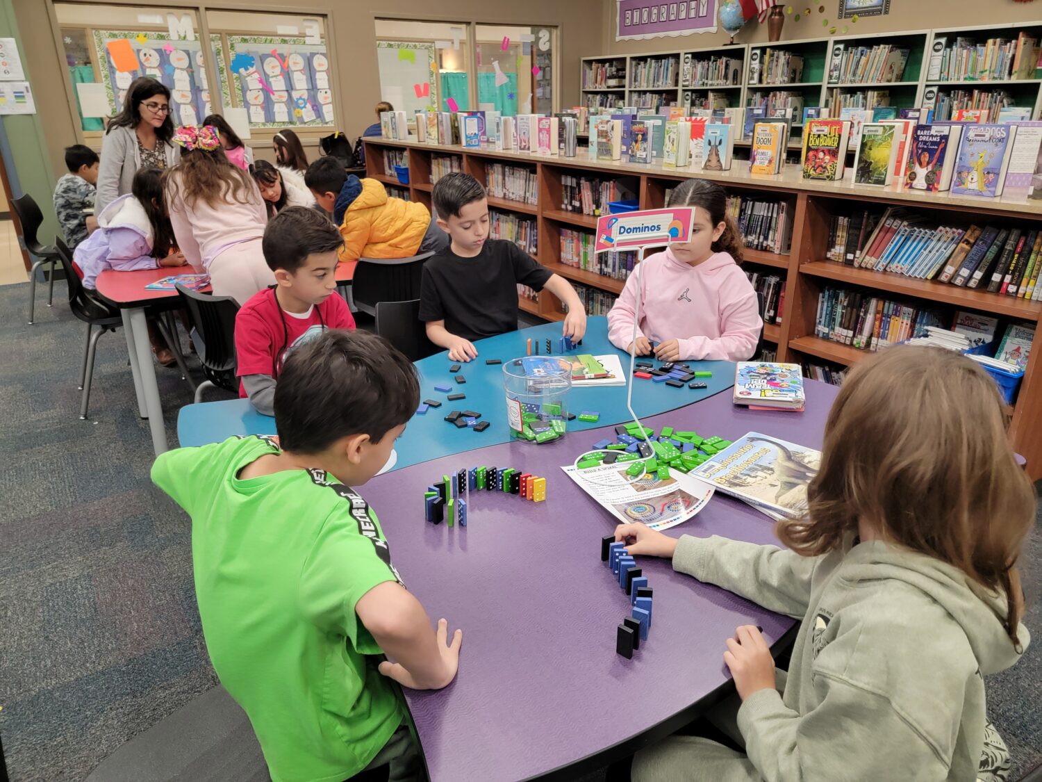 Students lining up colorful dominoes on a table in the library.