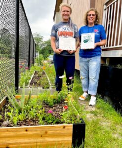 Coach Venessa Wallace (left) and Coach Dawn Davis (right) display their official recognition as a Monarch Waystation, standing by gardens designed and built by students in Peet Junior High’s Wildlife Management program.